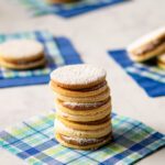 A stack of alfajores on a checkered bev nap with other alfajores in the background.